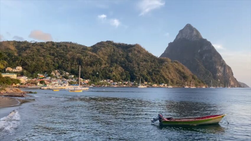 Fishing boat near the shore with the Pitons rising above a coastal village in St. Lucia