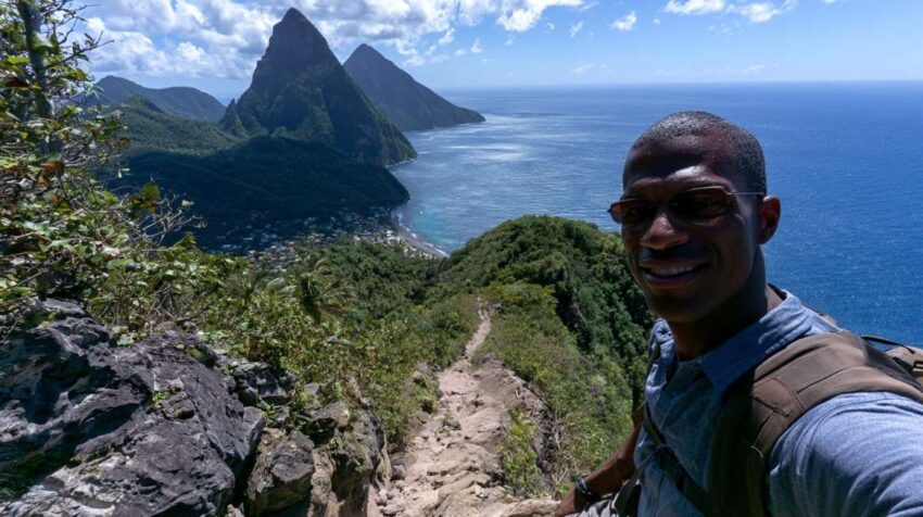 Hiker taking a selfie on a rocky mountain trail with Gros Piton, the Caribbean coastline, and the ocean in the background
