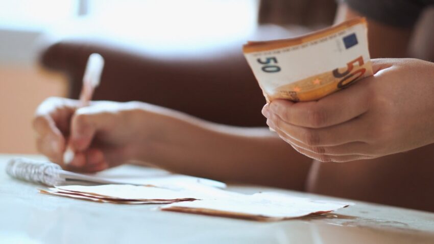 A person counts euro cash beside a notebook for a honeymoon budget