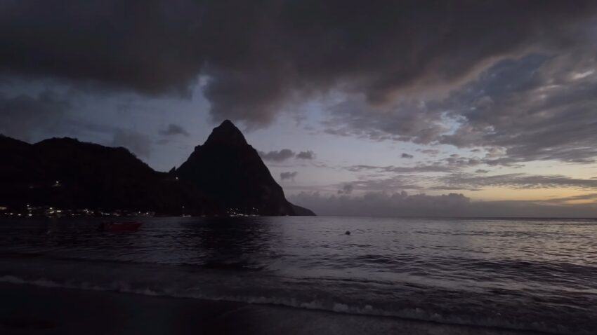 A dark St. Lucia beach at dusk with the Pitons over calm water