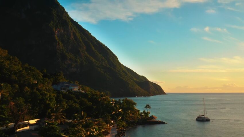 A sailboat sits near St. Lucia’s coast below a green mountain at sunset