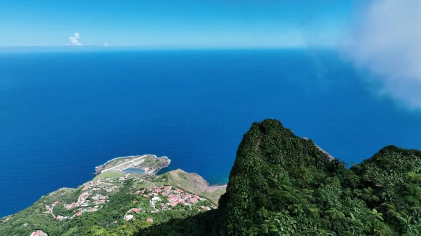 Aerial view of Saba’s green volcanic cliffs, village, airport, and blue Caribbean sea