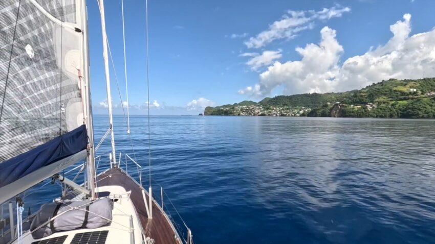 A sailboat moves across calm blue water near the green coast of St. Lucia