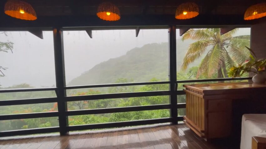 A rainy view of green St. Lucia hills and palm trees beyond a covered balcony
